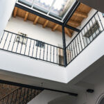 Perspectiva interior de la planta superior desde el salón en NintaiHome Los Venerables, destacando los techos y barandillas que mantienen la esencia sevillana.