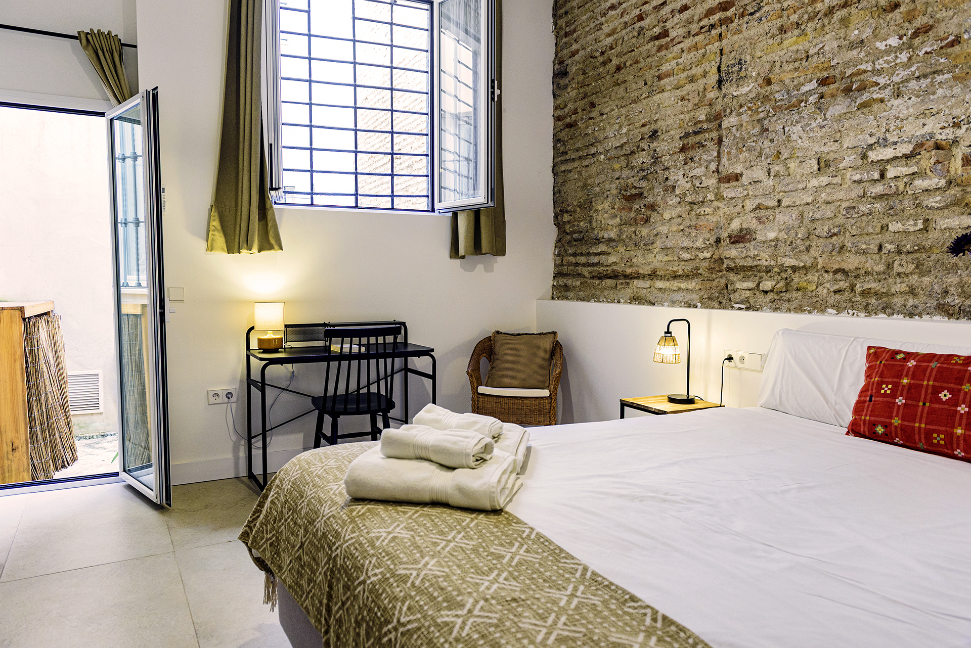 Dormitorio con acceso a patio en NintaiHome Los Venerables, resaltando su pared original de ladrillo visto y un diseño acogedor orientado al descanso.