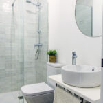 Interior de baño de diseño con acabados modernos y espejo redondo en NintaiHome Los Venerables.