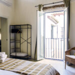 Dormitorio luminoso en planta alta de NintaiHome con balcón privado y vistas al patio interior tradicional sevillano.