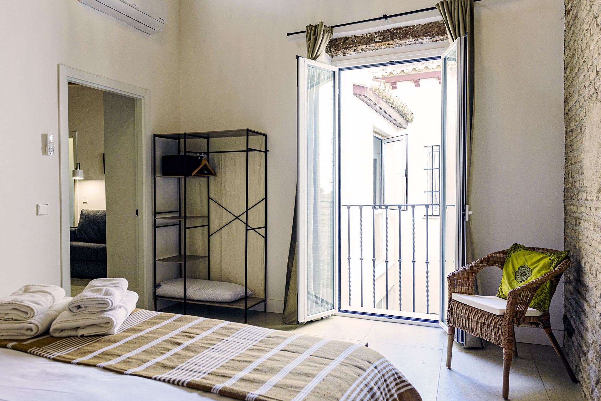 Dormitorio luminoso en planta alta de NintaiHome con balcón privado y vistas al patio interior tradicional sevillano.
