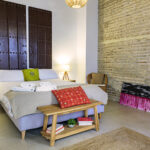 Dormitorio luminoso en la planta superior de NintaiHome en Sevilla, con una ventana-balcón que ofrece vistas a nuestro patio interior tradicional.