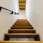 Modernas escaleras de madera con estructura metálica que conducen al solárium, con ventana al patio interior en NintaiHome, Sevilla.