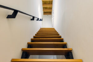 Modernas escaleras de madera con estructura metálica que conducen al solárium, con ventana al patio interior en NintaiHome, Sevilla.