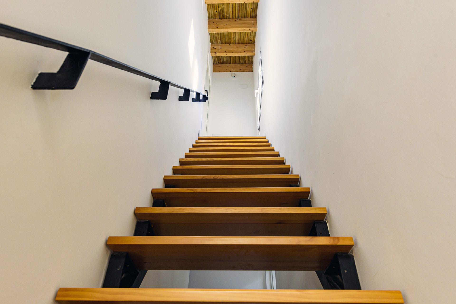 Modernas escaleras de madera con estructura metálica que conducen al solárium, con ventana al patio interior en NintaiHome, Sevilla.