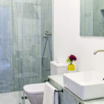 Interior de baño contemporáneo con lavabo cuadrado y ducha a ras de suelo, destacando la combinación de suelos clásicos y accesorios modernos en NintaiHome.