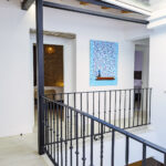 Pasillo luminoso en la segunda planta de NintaiHome Sevilla, con barandilla de hierro forjado y decoración de arte moderno.
