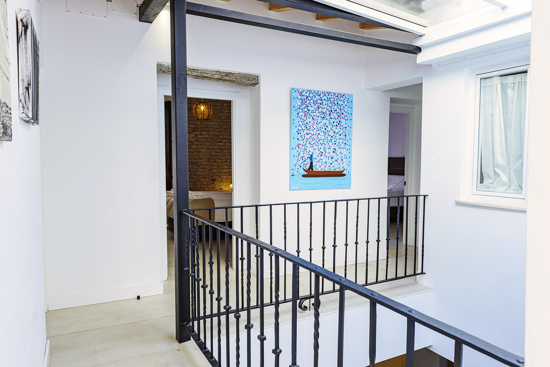 Pasillo luminoso en la segunda planta de NintaiHome Sevilla, con barandilla de hierro forjado y decoración de arte moderno.