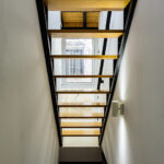 Vista de escaleras modernas de madera con estructura negra y ventana al patio interior en la planta alta de NintaiHome Sevilla.