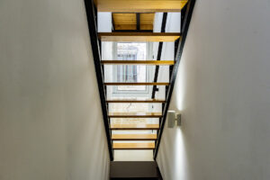 Vista de escaleras modernas de madera con estructura negra y ventana al patio interior en la planta alta de NintaiHome Sevilla.