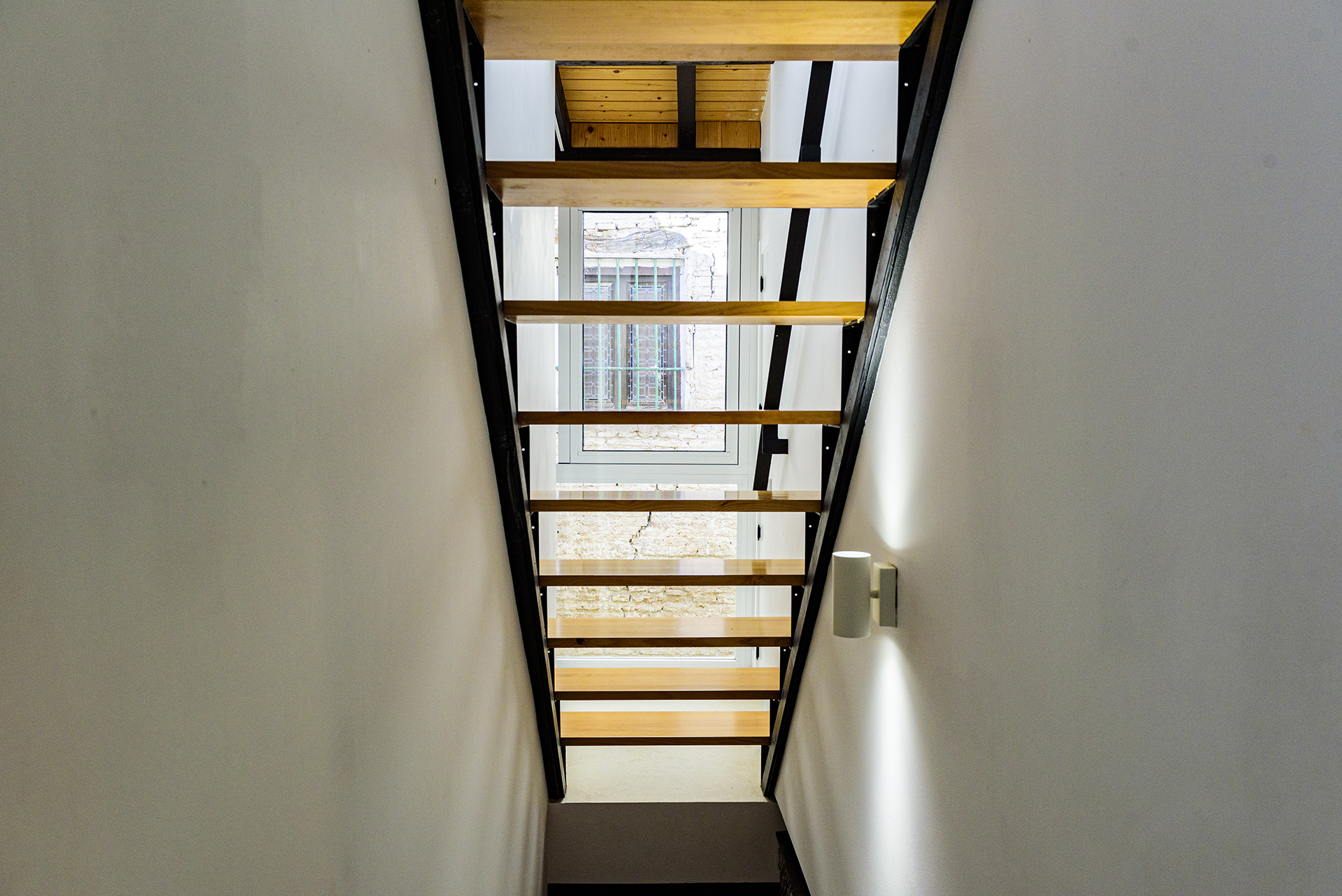 Vista de escaleras modernas de madera con estructura negra y ventana al patio interior en la planta alta de NintaiHome Sevilla.