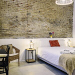 Dormitorio en planta baja de NintaiHome Los Venerables, destacando su pared de ladrillo histórico que colinda con el Hospital de los Venerables y acceso directo a un patio privado.