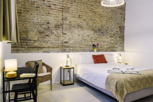 Dormitorio en planta baja de NintaiHome Los Venerables, destacando su pared de ladrillo histórico que colinda con el Hospital de los Venerables y acceso directo a un patio privado.